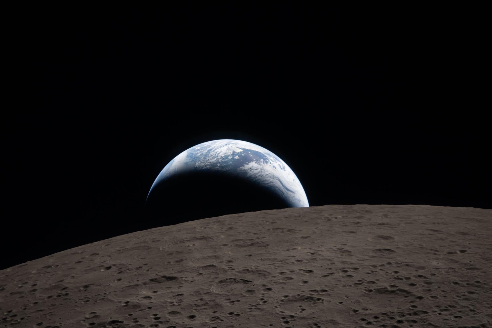 Earth setting behind the cratered Moon, photographed through the Orion spacecraft window