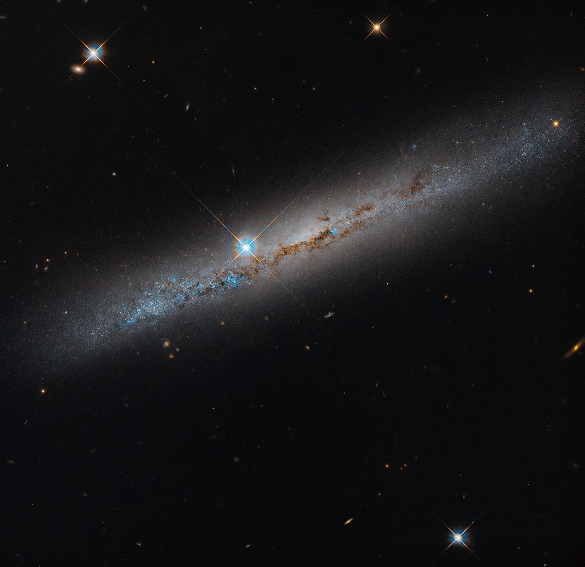 Hubble telescope image of edge-on galaxy NGC 1827 with blue regions, brown dust lanes and a bright foreground star